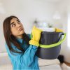 Shocked Woman Looks at the Ceiling While Collecting Water Which Leaks in the Living Room at Home. Worried Woman Holding Bucket While Water Droplets Leak From Ceiling in Living Room